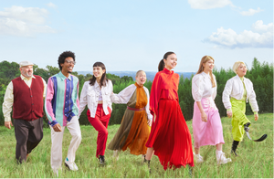 Group of people walking in a line on a grassy field with a blue sky and trees in the background