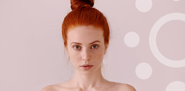 Woman with red hair styled in a bun against a light pink background with white circles.
